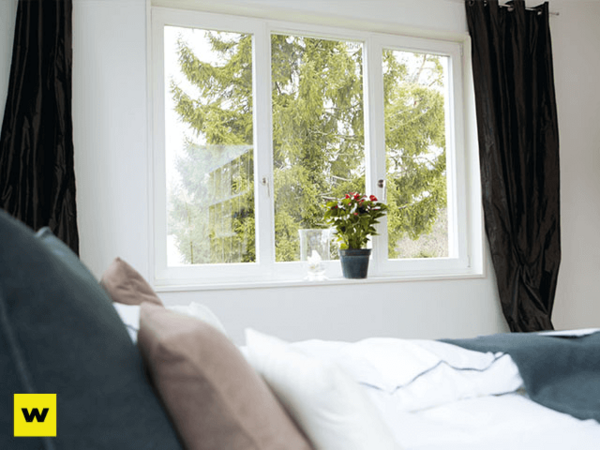 Helles Schlafzimmer mit großem Fenster, Blick ins Grüne und gemütlichem Bett.