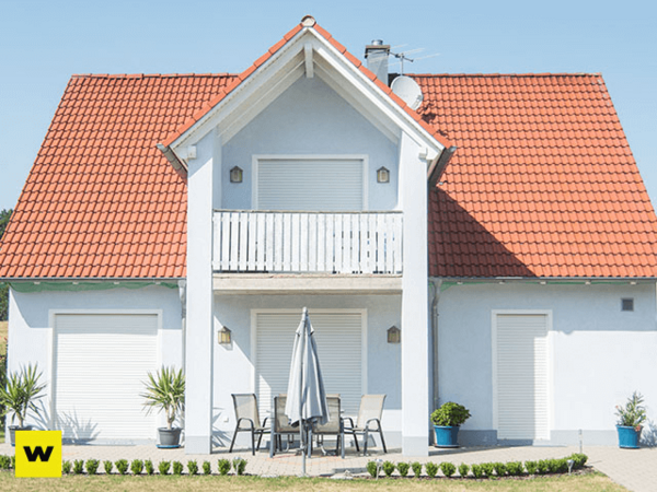 Modernes Einfamilienhaus mit rotem Dach, Rollläden und Terrasse im sonnigen Garten.